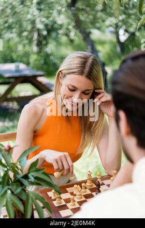 Donna positiva che gioca a scacchi con il ragazzo sfocato nel parco Foto Stock