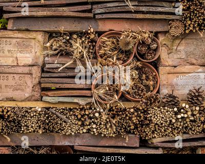 Bug hotel composto da mattoni impilati, tegole, pentole e ramoscelli di piante, in un giardino britannico. Foto Stock