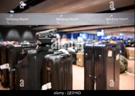 Amburgo, Germania. 23rd giugno 2022. "Aeroporto di Amburgo" è scritto su un nastro di barriera davanti a numerose valigie immagazzinate nell'area di ritiro bagagli. Centinaia di valigie, borse e carrozzine sono ancora impilate nell'area di ritiro bagagli dell'aeroporto e ci sono giorni per trovare i loro proprietari. Secondo l'aeroporto, questo è il cosiddetto bagaglio di corsa, che è arrivato ad Amburgo su un volo più tardi del passeggero. Credit: Jonas Walzberg/dpa/Alamy Live News Foto Stock