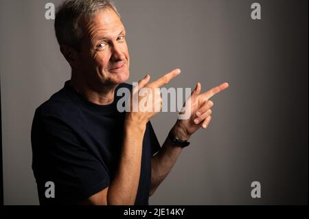 Uomo anziano sorridente in una maglietta blu, puntata, su sfondo grigio con spazio copia Foto Stock