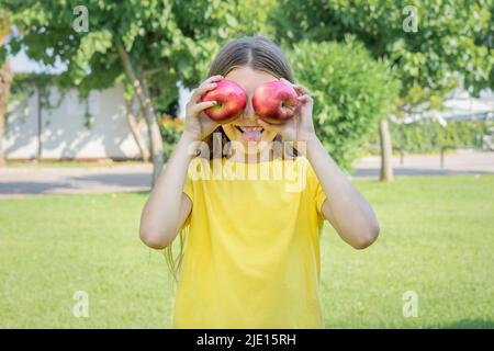 Una ragazza adolescente tiene due mele davanti al suo volto nel parco. Foto Stock