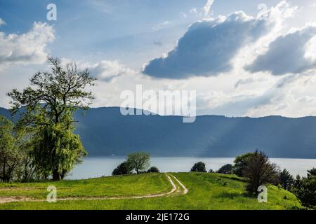 Stretto sentiero abbandonato trodden conduce attraverso verde prato erboso con vegetazione di montagna conduce a limpido e profondo lago intermontano, sullo sfondo di m Foto Stock