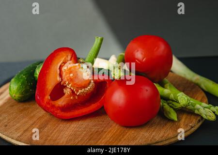 rami di asparagi verdi freschi, peperoni, pomodori e cetrioli su un asse di legno, sfondo grigio scuro, vista dall'alto. Concetto di trend di base con copia sp Foto Stock