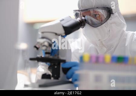 Scienziato in un abito protettivo che guarda attraverso un microscopio in un moderno laboratorio attrezzato Foto Stock