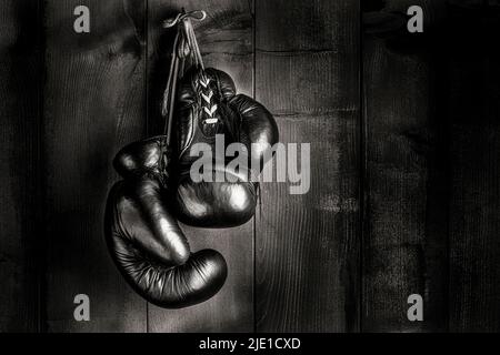 vecchi guanti da boxe appesi di fronte al rustico muro di legno Foto Stock