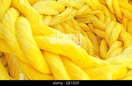 Corda colorata intrecciata spessa e resistente intrecciata intrecciata e intrecciata. Corda gialla spessa macro closeup posando in un mucchio. Il materiale robusto a lungo ritorto simboleggia l'unità Foto Stock