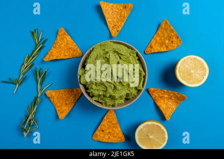 Composizione di guacamole con gli ingredienti per la sua creazione e il nachos per il suo consumo su sfondo blu Foto Stock