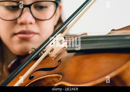 closeup latino caucasica donna con occhiali, ispirato violino da gioco, fuoco su archi e arco. Foto Stock
