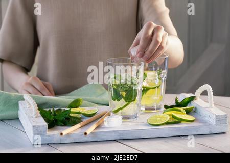 La ragazza prepara rinfrescanti cocktail estivi alla frutta mojito con lime e menta. Foto Stock