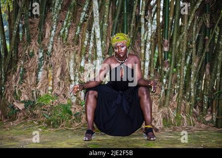 Donna tribale africana seduta nella giungla con pittura facciale e headdress Foto Stock