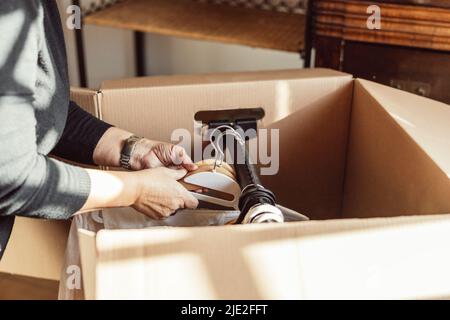 donna irriconoscibile che mette i vestiti sugli appendiabiti all'interno di una scatola mobile di cartone Foto Stock