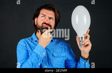 Nascita di idee. Uomo pensivo con lampadina. Il tizio con bearded premuroso tiene la lampadina e il pensiero. Foto Stock