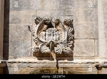Una maschera singola sorronde uno dei rubinetti della grande Fontana di Onofrio nella città vecchia di Dubrovnik Foto Stock