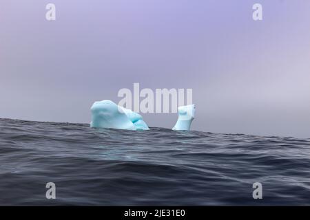 L'onda si schiantando contro un piccolo iceberg che galleggia in mare Foto Stock