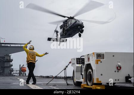 Un direttore di velivolo della Marina degli Stati Uniti guida un pilota del 33rd Rescue Squadron HH-60G Pave Hawk dopo il decollo da una nave navale degli Stati Uniti, 17 giugno 2022. I registi di aerei della Marina aiutano a dirigere il movimento e l'individuazione degli aerei sia in mare aperto che in mare aperto. (STATI UNITI Air Force foto di Senior Airman Stephen Pulter) Foto Stock