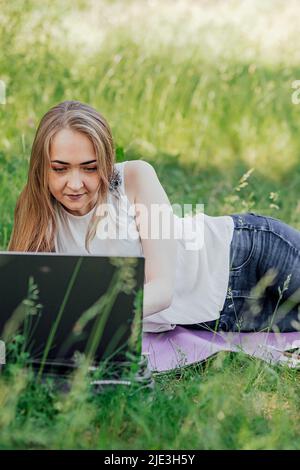 Sul banner, una giovane ragazza lavora con un computer portatile all'aria aperta nel parco, seduto sul prato. Il concetto di lavoro a distanza. Lavora come freelance. T Foto Stock