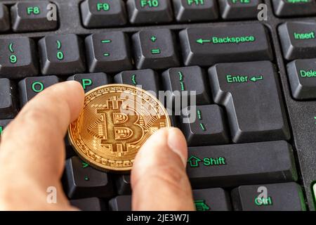 Mano che tiene il bitcoin adagiato sulla tastiera del computer, criptovaluta per il pagamento digitale Foto Stock