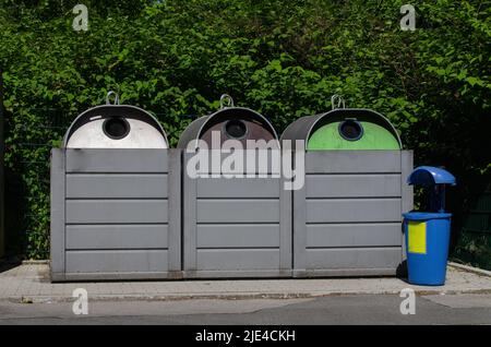 fila di tre banchi di bottiglie / punto di raccolta del riciclaggio del vetro per il riciclaggio di vetro bianco, marrone e verde e un cestino per sacchetti di plastica usati, ecc. Foto Stock