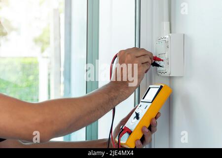 Un elettricista che utilizza un misuratore digitale per misurare la tensione su una presa a muro. Foto Stock