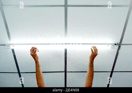 Primo piano di una mano di un uomo che installa una lunga lampadina a LED sul soffitto. Foto Stock