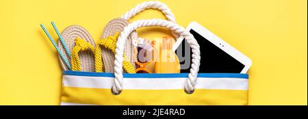 Accessori per il nuoto - borsa da spiaggia alla moda con strisce, occhiali neri, tavoletta bianca, foglia di palma, flop giallo su sfondo giallo Flat lay Top view Estate, viaggio, vacanza concept. Foto Stock