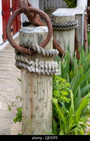 Palo di legno con anelli di ferro arrugginiti sulla parte superiore e corda da pesca avvolta intorno a diversi pali su bacino di legno su Cape Cod Foto Stock