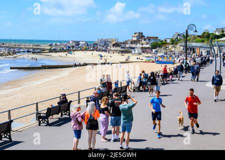 Lyme Regis, Dorset, Regno Unito. 25th giugno 2022. UK Meteo: I visitatori e la gente del posto fanno il meglio di incantevoli incantesimi caldi e soleggiati in una giornata calda, ma blustery alla stazione balneare di Lyme Regis. Si prevede che il sole si rompa più tardi, poiché la pioggia e il tempo tuono vengono dall'Occidente portando in condizioni più umide e mutevoli. Credit: Celia McMahon/Alamy Live News Foto Stock