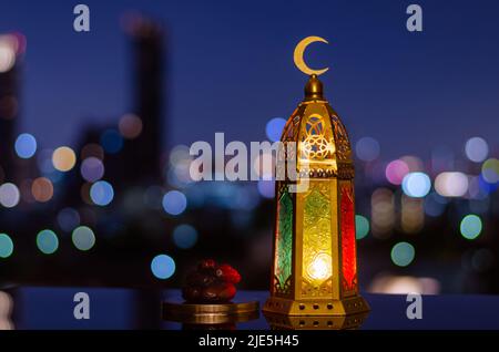Lanterna che ha il simbolo della luna sulla parte superiore e un piccolo piatto di datteri frutto per la festa musulmana del mese santo di Ramadan Kareem e l'anno nuovo islamico conc. Foto Stock