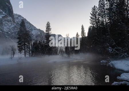 La valle di Yosemite è circondata da un sottile strato di nebbia che si estende sul fiume merced, fornendo un'atmosfera inquietante intorno al tramonto. Foto Stock