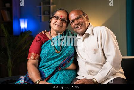 Ritratto girato di coppia anziana felice abbracciandosi a vicenda guardando macchina fotografica a casa- concetto di rapporto, felicità e legame di famiglia Foto Stock