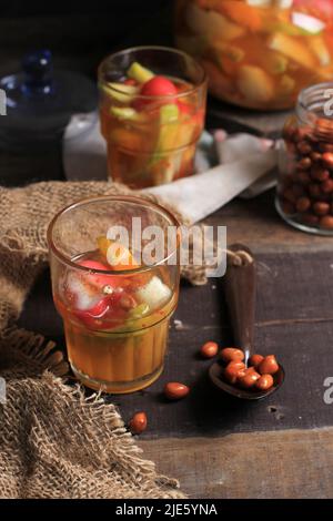 Asinan Buah Bogor o Rujak Buah, Pickle di frutta a fette di frutta tropicale fresca su zuppa rossa dolce, sour e piccante. Sormontato da Famo di arachidi fritte Foto Stock