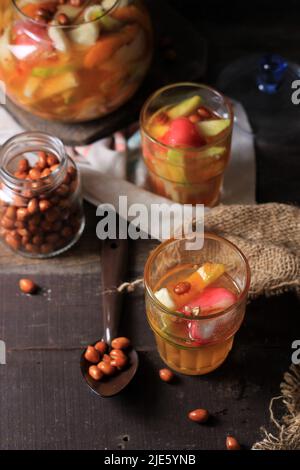 Asinan Buah Bogor o Rujak Buah, Pickle di frutta a fette di frutta tropicale fresca su zuppa rossa dolce, sour e piccante. Sormontato da Famo di arachidi fritte Foto Stock