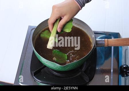 Chef femminile aggiungere foglie di lime e limongrass, processo di cottura a Rawon, manzo indonesiano Black Soup. Cucina Backstage in cucina Foto Stock