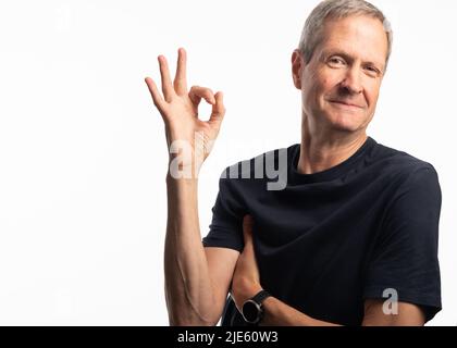 Un uomo anziano attivo in una maglietta blu con un atteggiamento positivo e sorridente su sfondo bianco Foto Stock