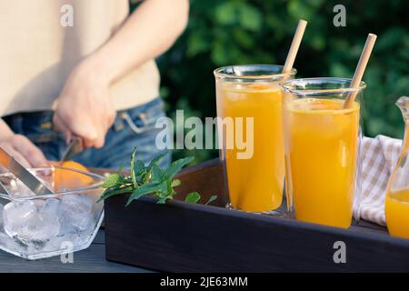 Ragazza che cucinano cocktail d'arancia estate con menta e cubetti di ghiaccio all'aperto, fuoco selettivo. Foto Stock
