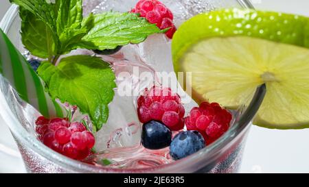 Rinfrescante cocktail estivo con ghiaccio, lime e frutti di bosco in un bicchiere di paglia. Foto Stock