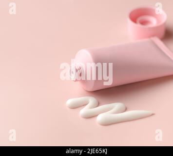 Pulire il tubo crema corpo viso di colore rosa con tappo aperto e prodotto tessuto crema spremuto su sfondo color carne Foto Stock