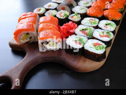 Vista dall'alto di sushi con salmone, formaggio cremoso, caviale, chuka su un tagliere di legno scuro. Sushi roll fritto con salmone - cibo giapponese. Sushi r Foto Stock