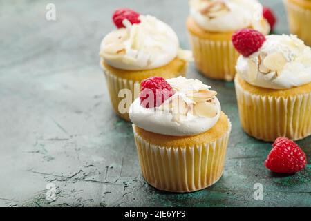 Muffin ai frutti di bosco dolci con panna, lamponi e mandorle su sfondo verde scuro. Banchetto, picnic, compleanno. Libro di ricette. Ristorante e casa co Foto Stock