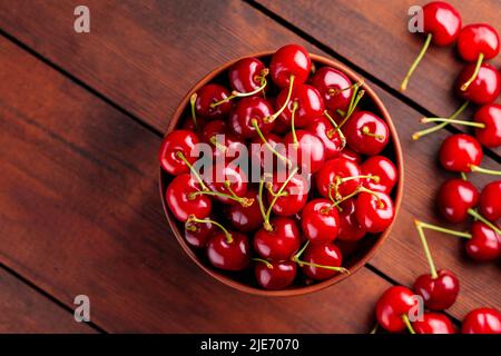 Ciliegie mature in una ciotola di argilla. Ciliegie rosse su un tavolo di legno. Concetto di cibo vegano sano. Vista dall'alto. Spazio di copia Foto Stock