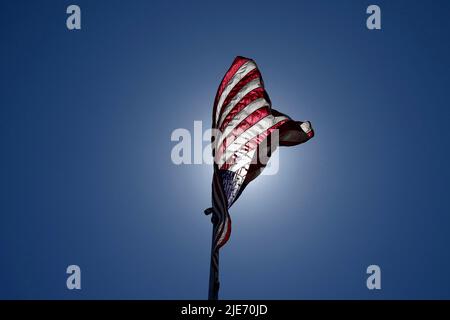 Una vista ad angolo basso di una bandiera americana riaccesa dal sole che soffia nel vento. Foto Stock