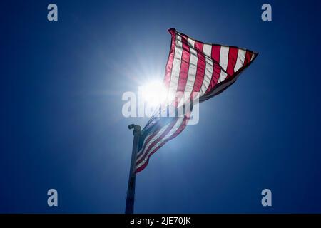 Una vista ad angolo basso di una bandiera americana riaccesa dal sole che soffia nel vento. Foto Stock