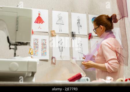 Il fashion designer sviluppa schizzi di design di abbigliamento. L'artista crea abiti da donna. Lavorare su misura con il tessuto. Foto Stock