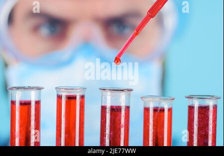 Medico in occhiali protettivi gocciola liquido rosso in provette. Campione di sangue. Ricerca di laboratorio. Foto Stock