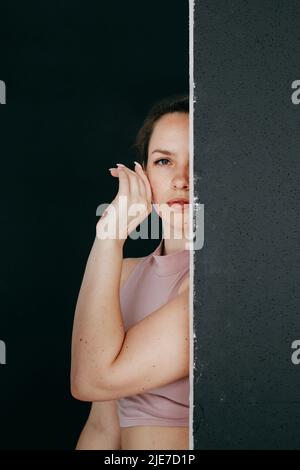 Una bella brunetta si sbirca dietro uno schermo nero. Primo piano ritratto di una giovane ragazza che tiene la mano al suo volto. Foto Stock