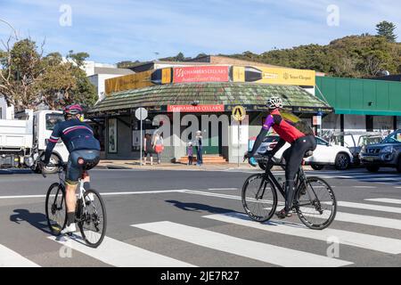 Due uomini in bicicletta o bici da strada a un incrocio pelican nel sobborgo di Avalon Beach di Sydney in un giorno d'inverno, NSW, Australia Foto Stock