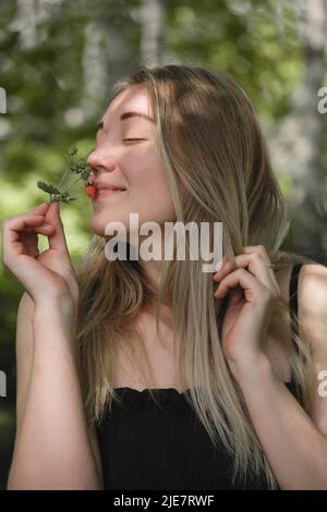 Donna che odora fragole selvatiche nella foresta. Bacche rosse mature nella natura piena di vitamine. Attività estive per il tempo libero per le persone all'aperto. Primo piano Foto Stock