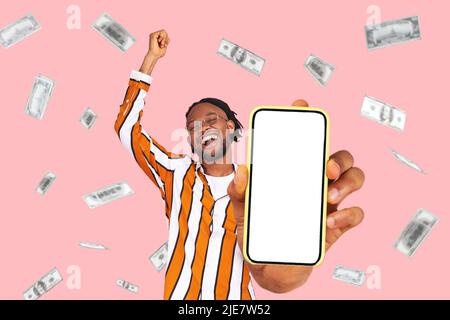 Investimento in linea, vincitore overjoyed l'uomo ricco e i dollari guadagnano i soldi. Ritratto di stupito giovane uomo che mostra mobile vuoto display e celebrare la sua vittoria. Indoor isolato su sfondo rosa. Foto Stock