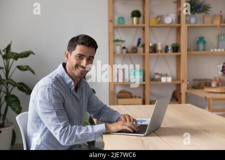 Il freelance uomo si siede alla scrivania con il computer portatile che fissava la fotocamera Foto Stock