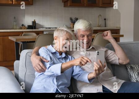 Coppia anziana che sta fissando al grido del telefono cellulare con la gioia celebrare il successo Foto Stock